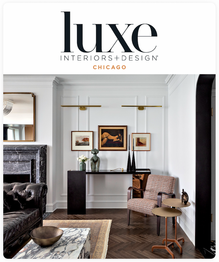 A living room with a black leather couch, a marble coffee table, and a black console table with artwork and sculptures. The room has a white fireplace and a wooden floor.